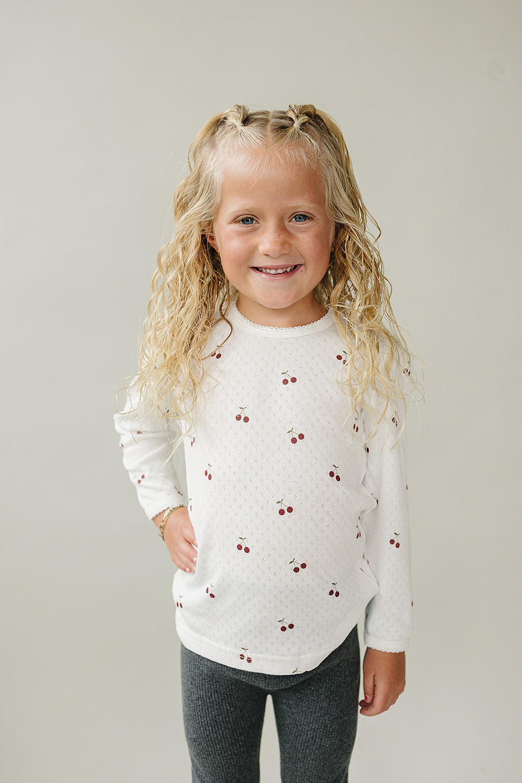Young girl wearing a white long-sleeve shirt with red patterns against a plain background