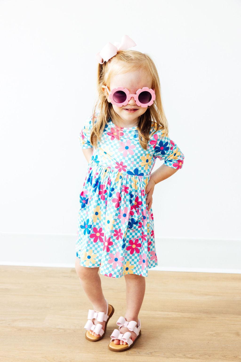 Young girl wearing a colorful floral dress and pink sunglasses on a white background