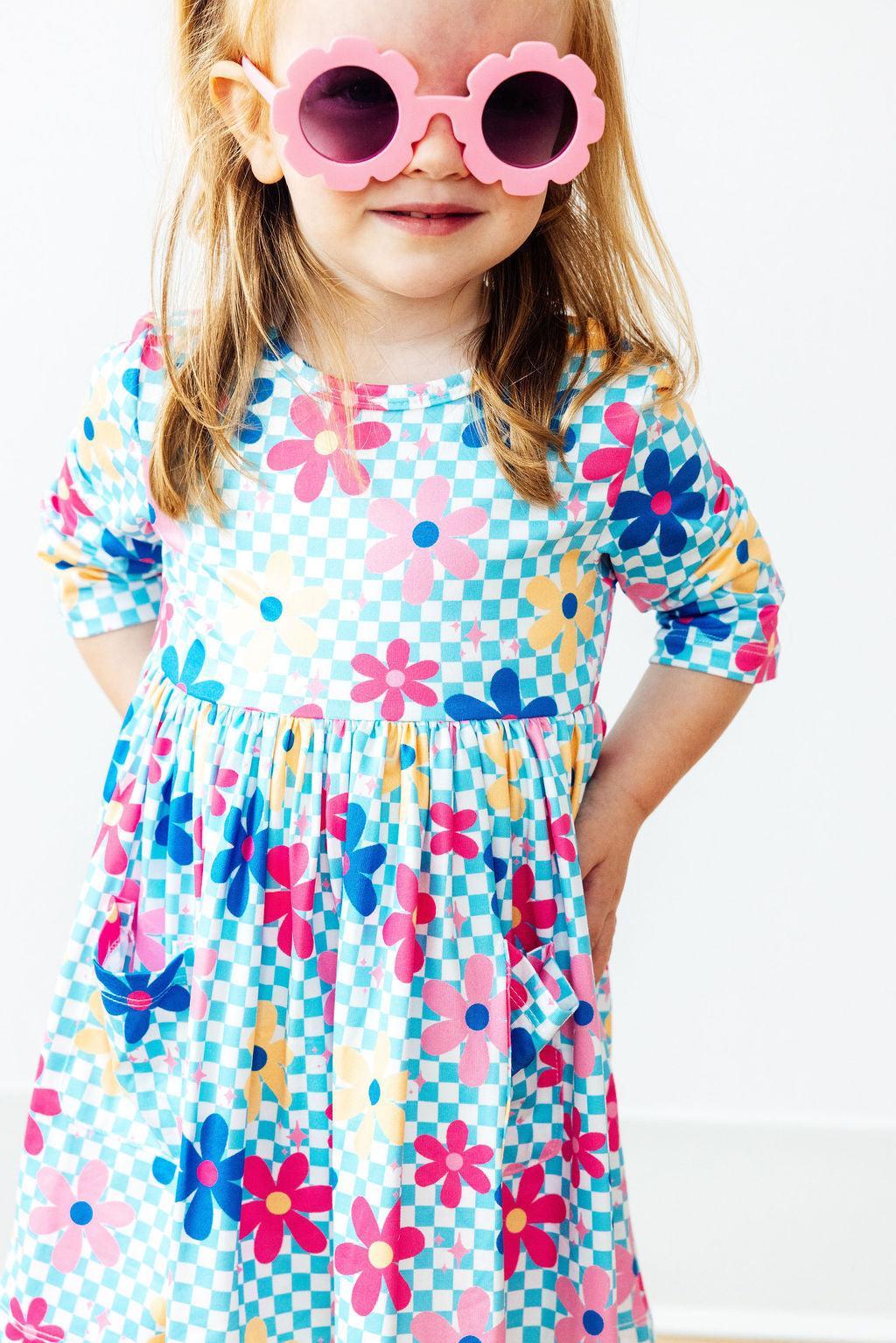 Child wearing a colorful floral dress and pink sunglasses on a white background