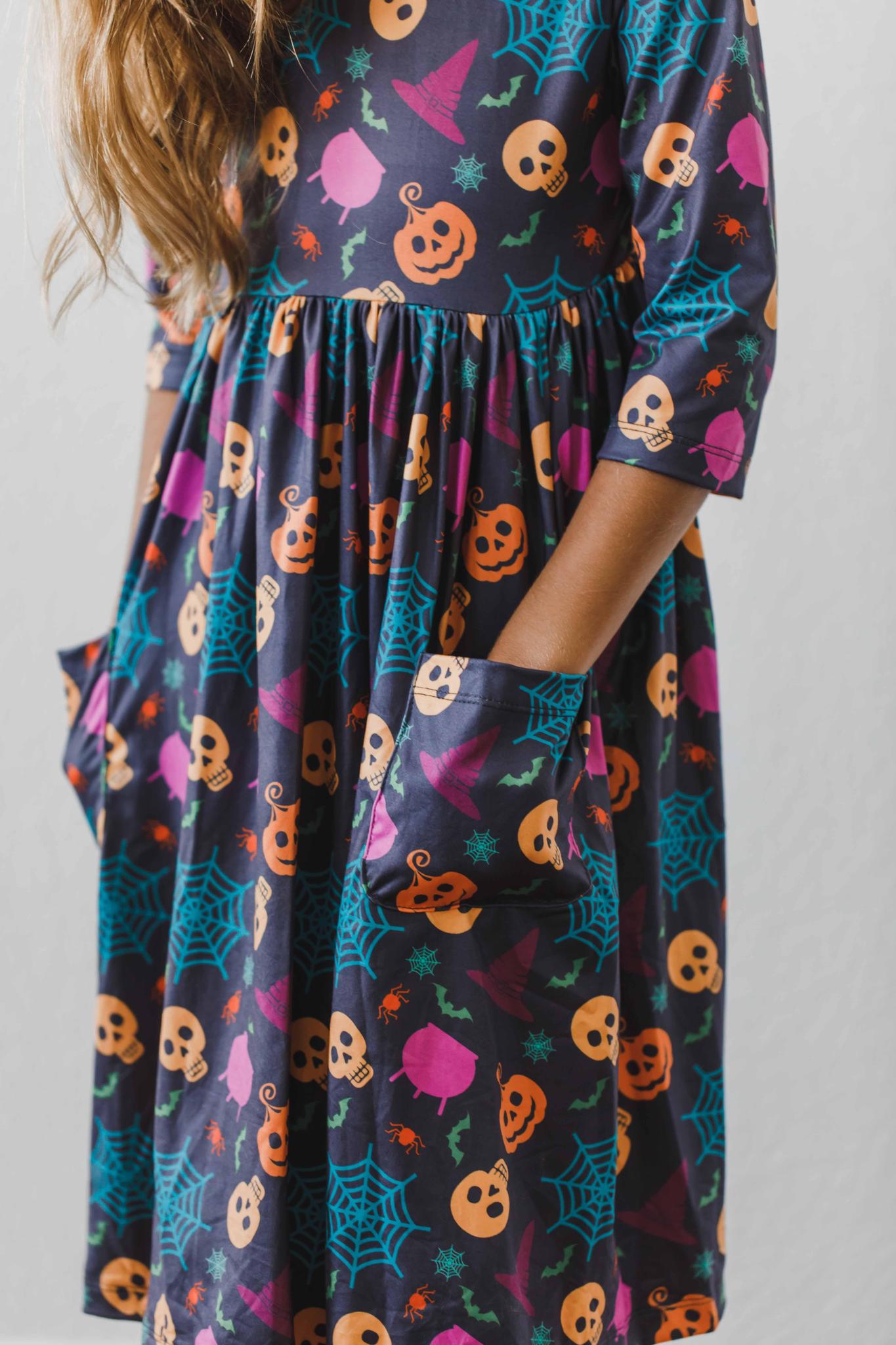 A child wearing a long sleeve dress with a colorful pattern featuring pumpkins and spiders.